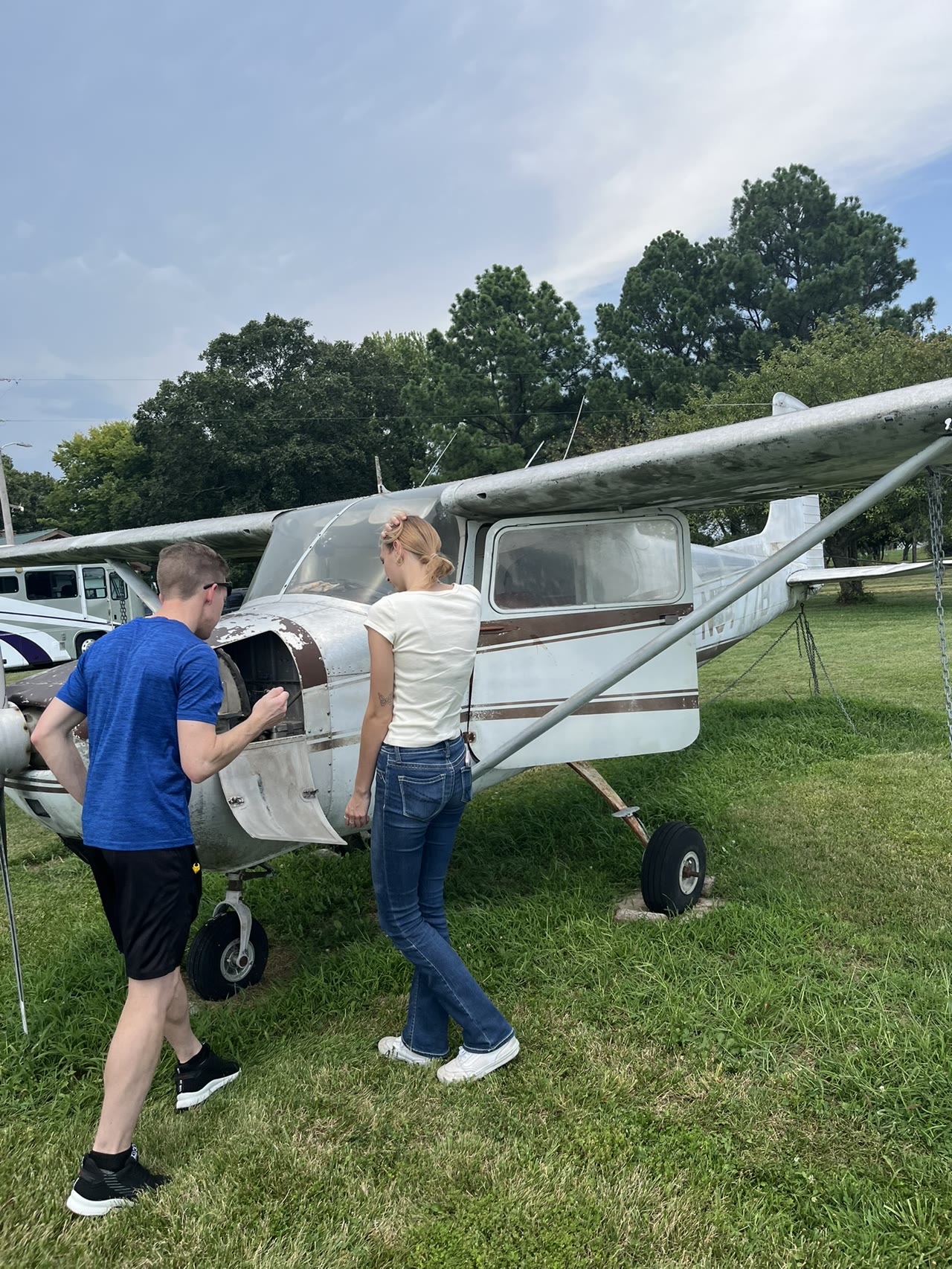 Two people examining the left side of N8777B during an initial walk-around on grass.