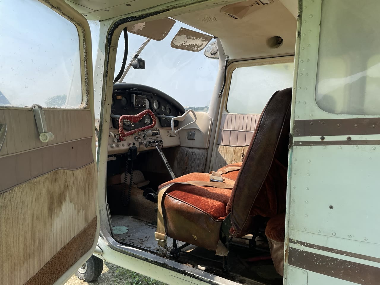 Wide view through the cabin of N8777B after initial professional cleaning, showing aged red seating and original interior surfaces.